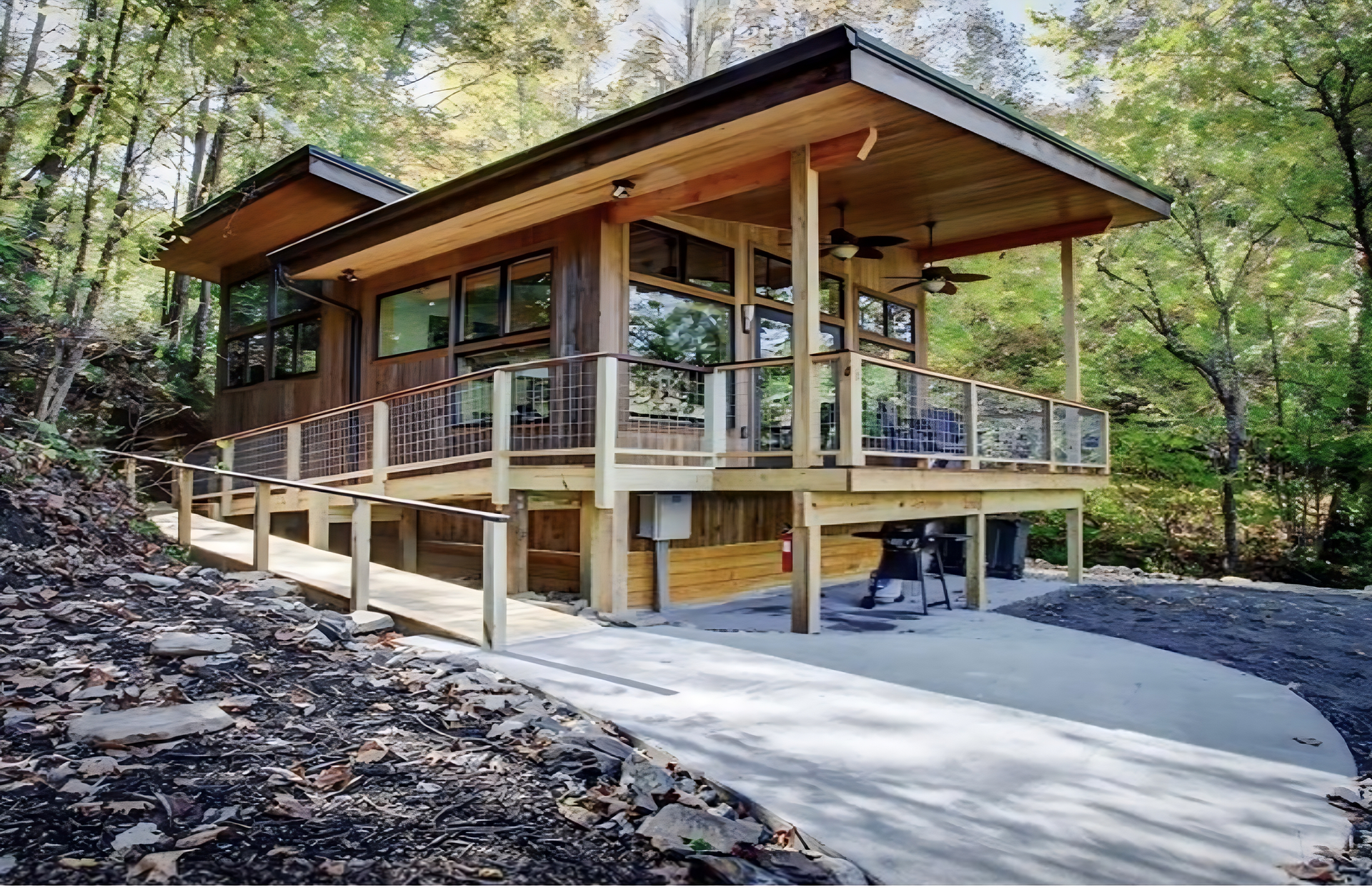 Wooden cabin with a ramp and deck in a wooded setting.
