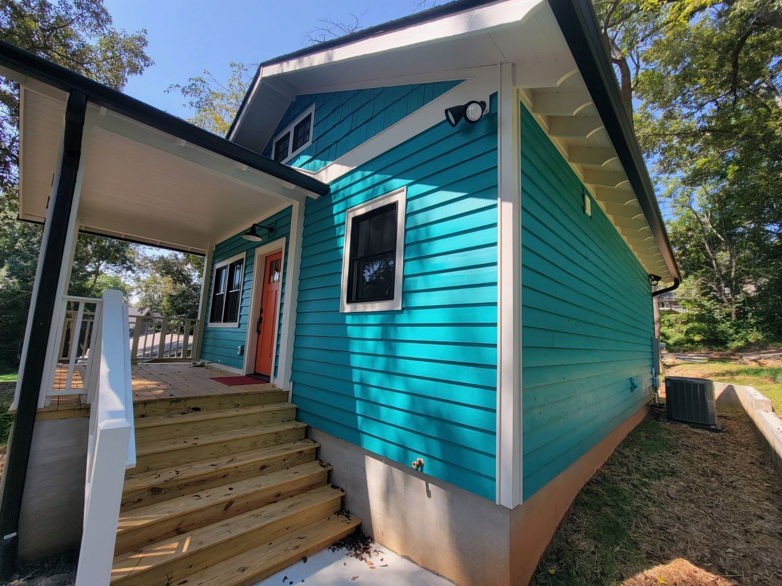 Turquoise house exterior with front steps, white trim, and a covered porch under trees