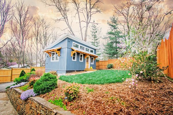 A small house is sitting in the middle of a backyard next to a wooden fence.