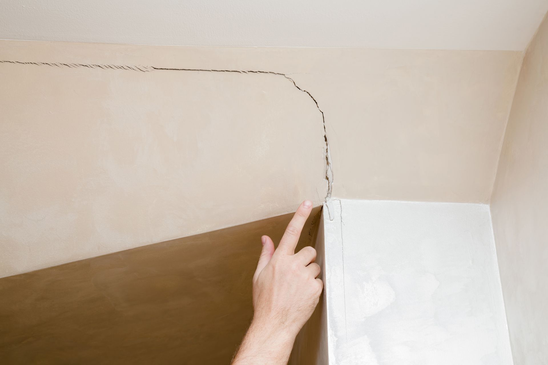 Finger pointing to a cracked ceiling corner above a wall