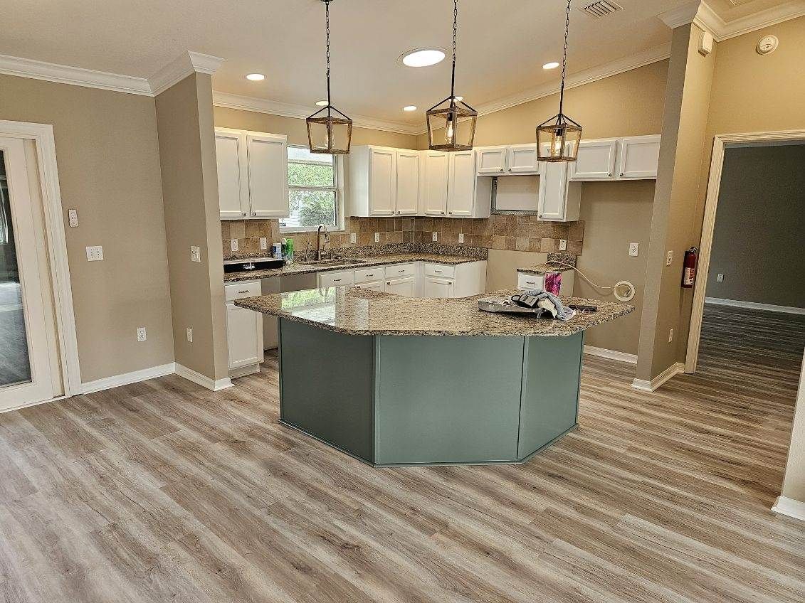 A kitchen featuring white cabinets, a green-painted island with a granite countertop, and light wood-look flooring.