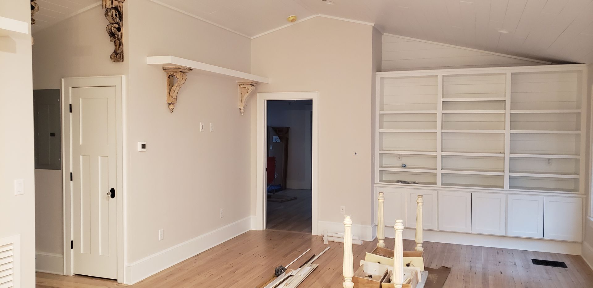 Interior view of a room with unfinished walls and built-in white shelves. There is a wooden floor.