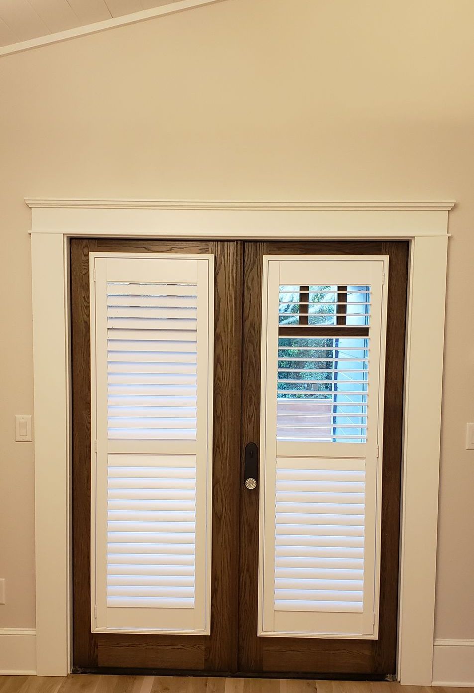 A pair of sliding glass doors with white shutters in an empty room.