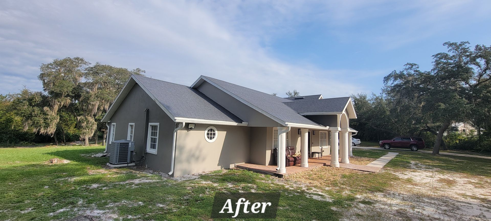 A house with a gray roof is sitting in the middle of a grassy field.