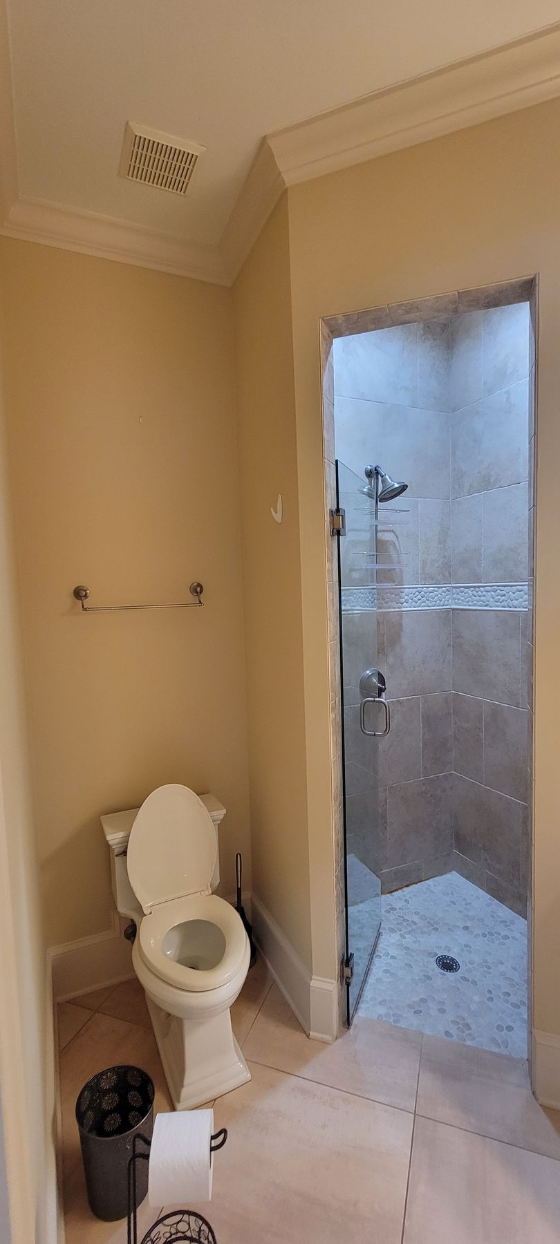 A bathroom with a toilet , shower , and trash can.