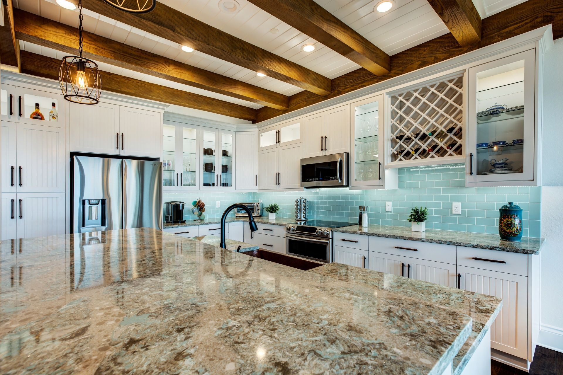 Modern kitchen with white cabinets, stainless steel appliances, marble island, and exposed wood ceiling