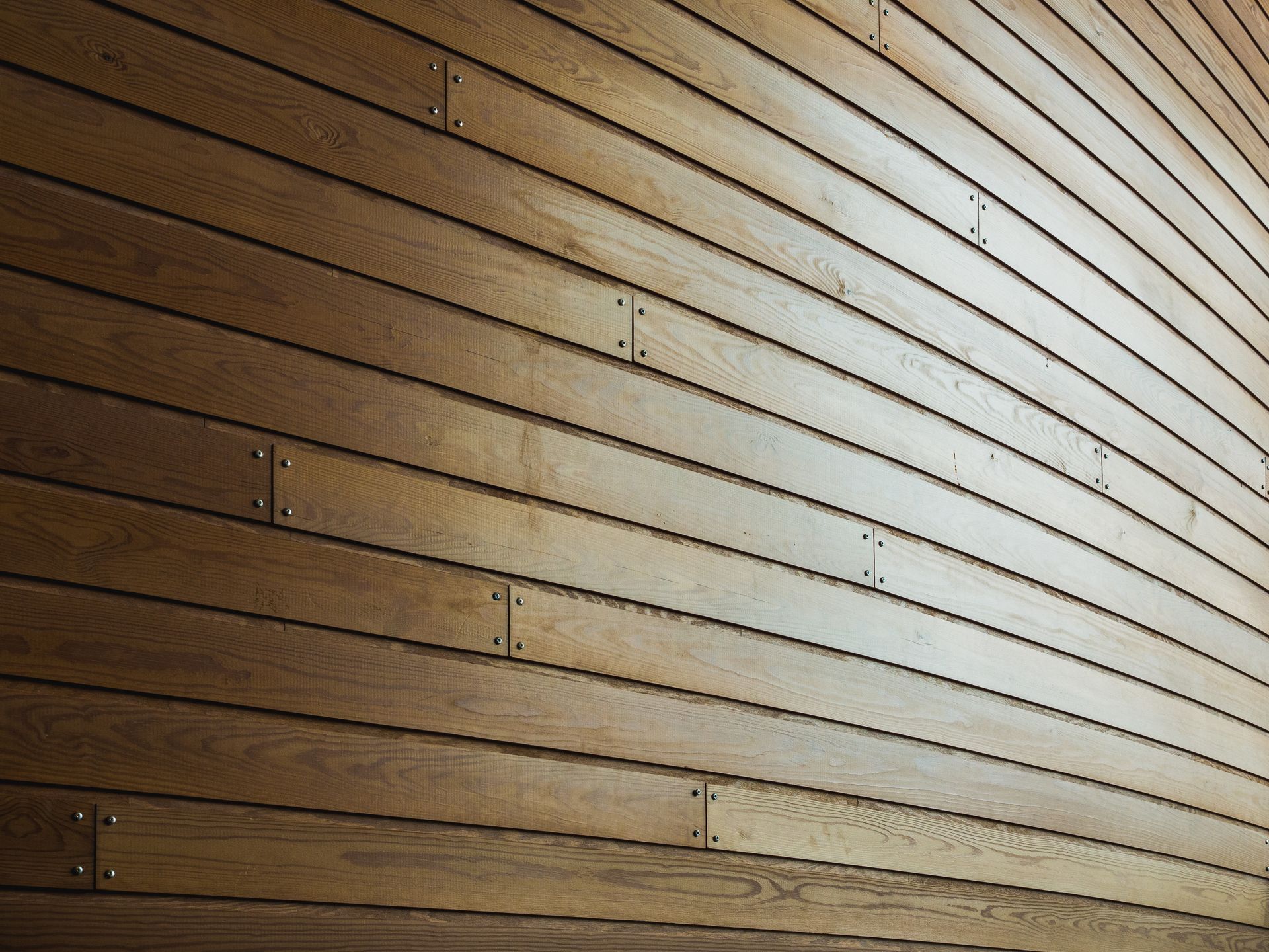 Wooden slat wall with a warm brown finish and bright light reflecting across the right side