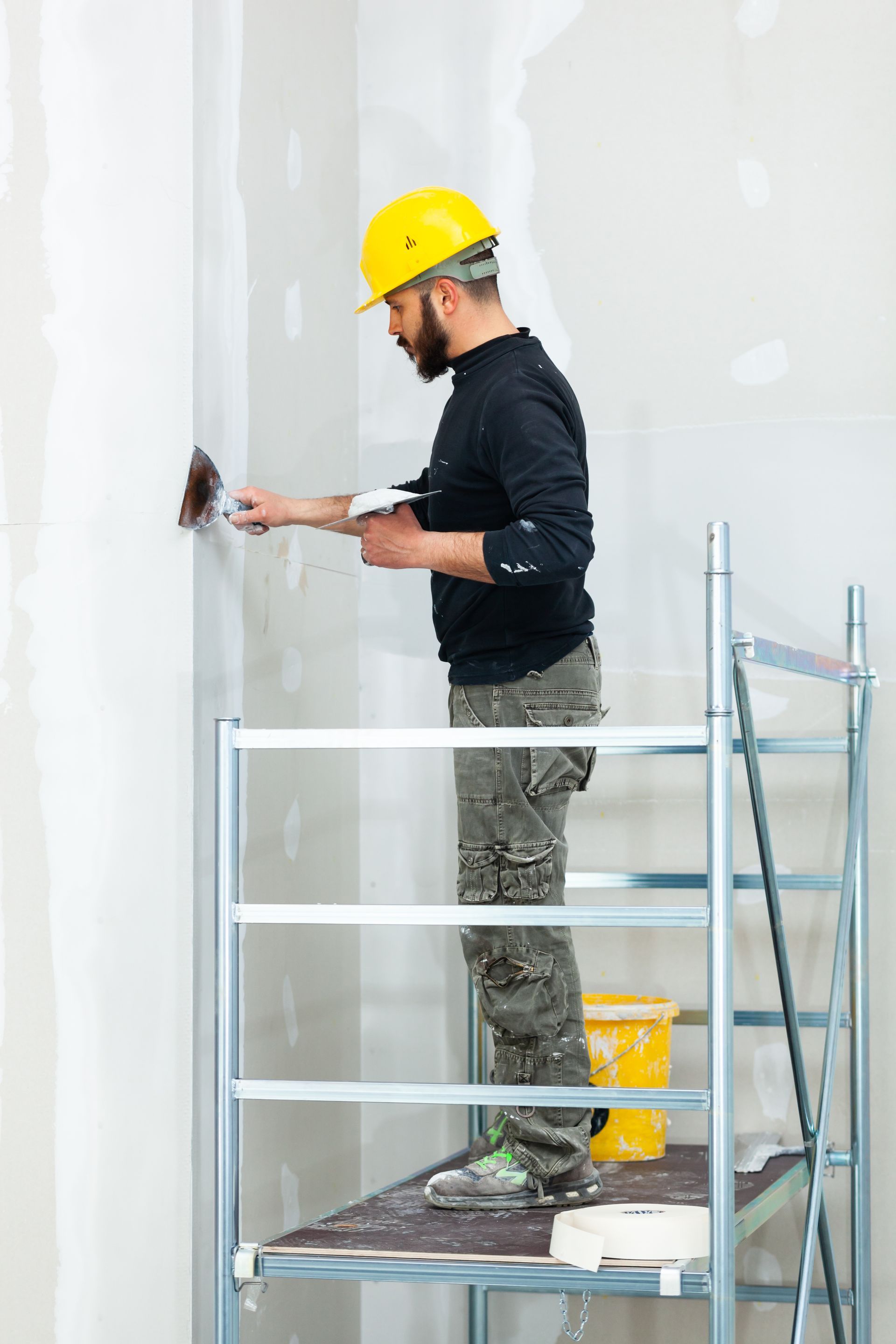 A man is standing on a scaffolding painting a wall.