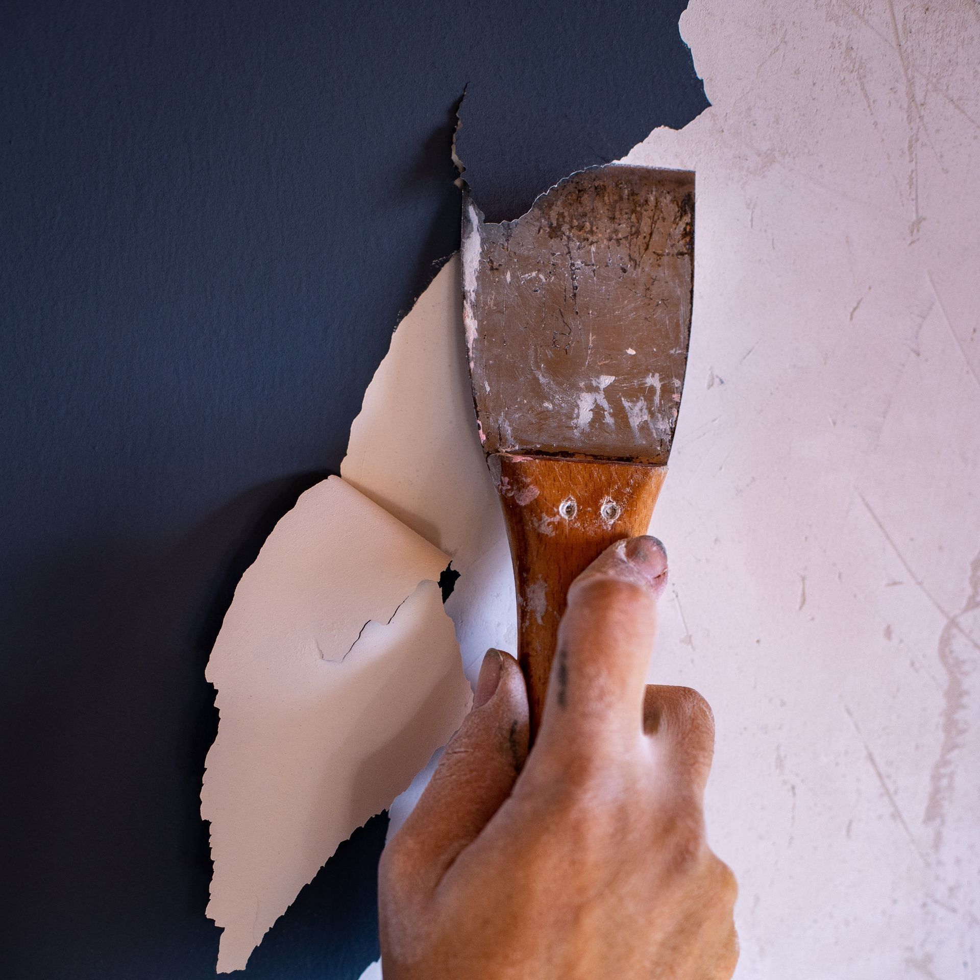 A person is holding a spatula in front of a black wall
