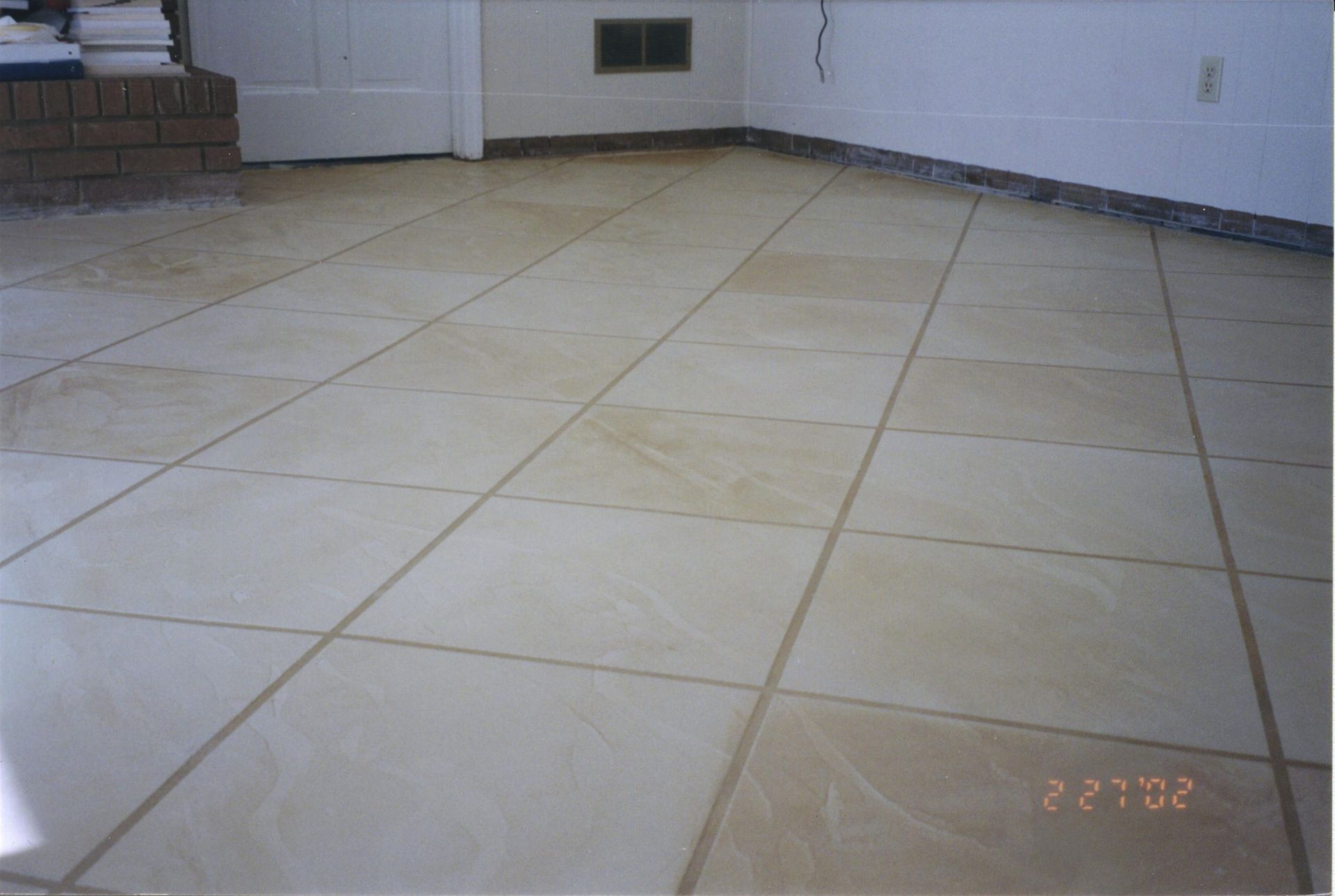 Empty tiled floor in a room with white walls and a door in the background.
