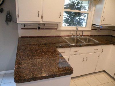 Kitchen with dark granite countertop, white cabinets, and a double sink under a window.