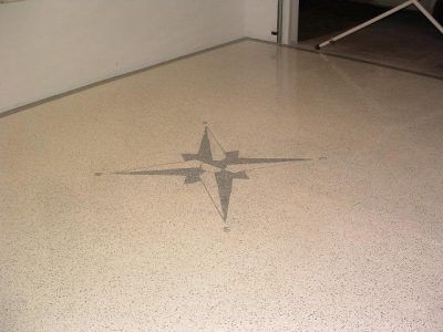Small compass rose tile design on a speckled beige floor near a wall.