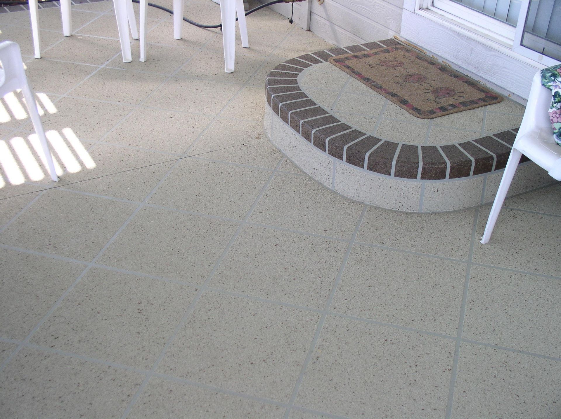 Patio floor with a curved brick planter near white chairs and a door.