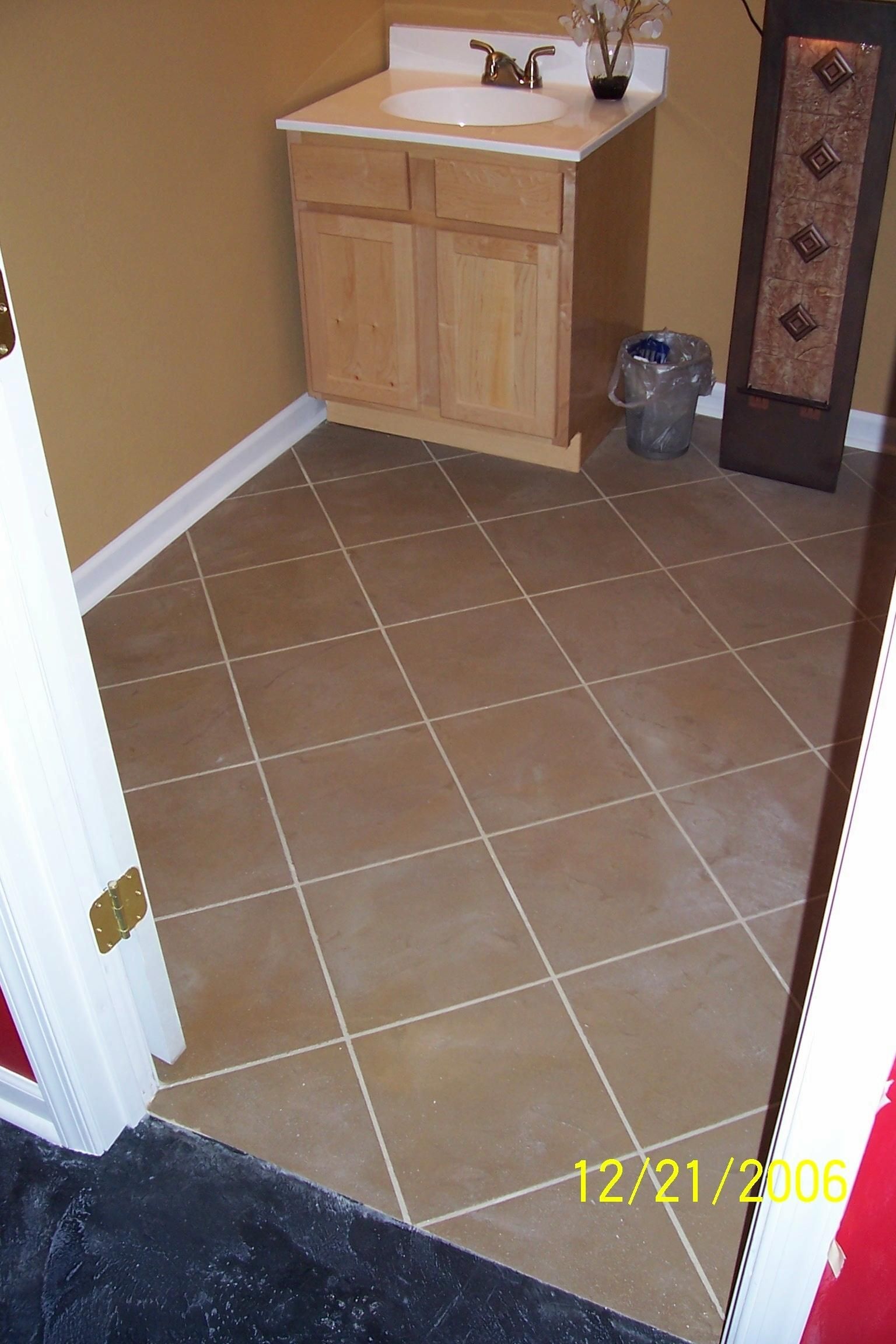 Bathroom with tan tiled floor, wood vanity, and toilet paper holder near the door.