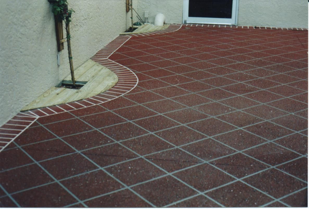 Red tiled patio with a curved beige border beside a stucco wall and doorway.
