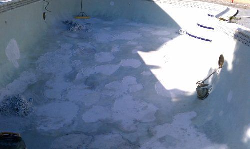 Empty swimming pool being cleaned, with patchy residue and a person using a hose on the right side