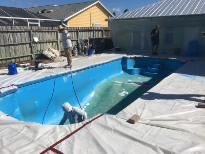 Workers cleaning a drained backyard pool covered with white tarp under sunny skies
