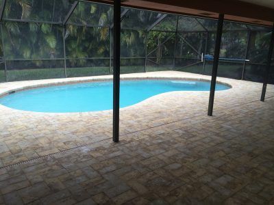 Covered outdoor pool with turquoise water, stone deck, and screened enclosure under a roof