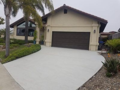 Suburban house with a dark garage door, wide light concrete driveway, and palm trees in front