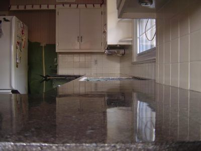 Floodwater covering a kitchen floor, reflecting cabinets and a window.