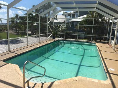 Screened-in backyard pool with turquoise water and a metal handrail, beside a patio and lawn.