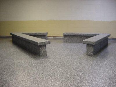 Two concrete benches facing each other in a sparse indoor room with a gray floor and beige wall.