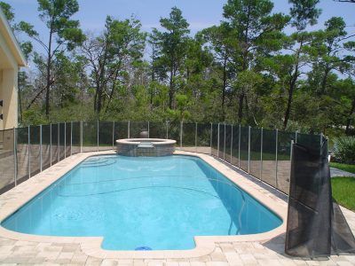 Empty backyard swimming pool with a circular hot tub and surrounding fence under trees