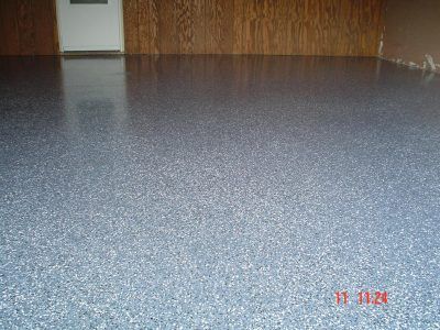 Empty room with speckled blue floor, wood-paneled wall, and a white door in the back.