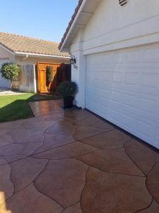 Stamped concrete driveway beside white garage, leading to a house entrance with a wooden front door.
