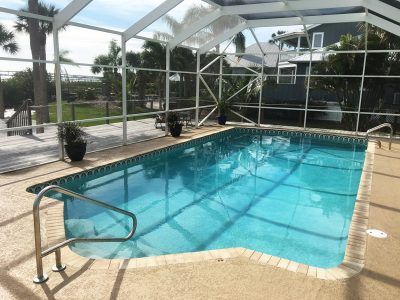 Covered backyard swimming pool with blue water and metal handrails, surrounded by a screened patio.