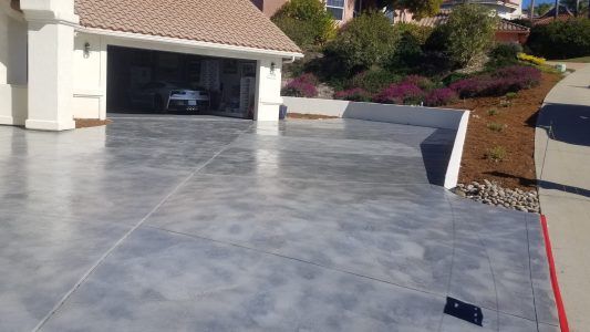 Concrete driveway with a garage and house, showing a smooth gray stamped surface and landscaped yard.