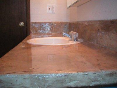 Bathroom sink and countertop with water damage, showing stains and discoloration near the faucet and wall.