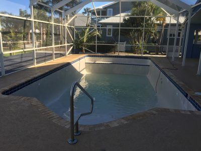 Empty covered backyard pool with a handrail and safety fence, viewed in daylight