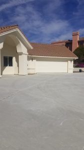 Suburban house with a red tile roof and a large concrete driveway under a blue sky