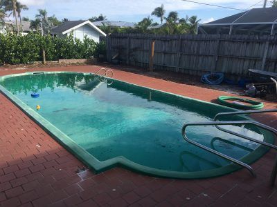 Backyard swimming pool with brick deck, hose, and fence under a sunny sky