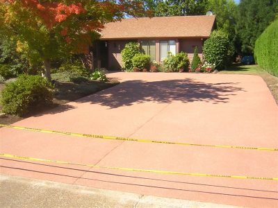 Driveway with yellow caution tape in front of a suburban house and trees.