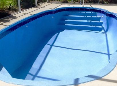 Empty blue swimming pool with steps and a ladder in bright sunlight