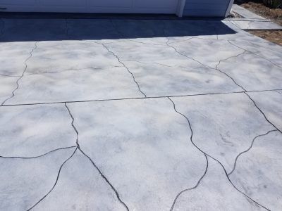 Cracked concrete driveway in front of a garage, viewed from above.