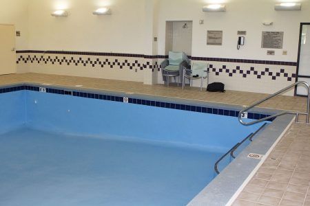 Indoor swimming pool with blue water, tiled deck, and pool lift chair by the wall