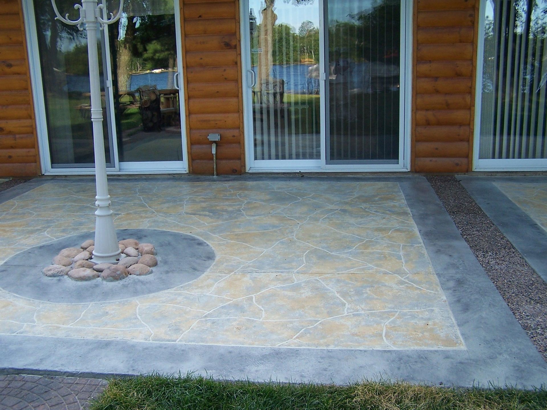 Stone patio with a central umbrella pole and sliding glass doors on a log-cabin-style house