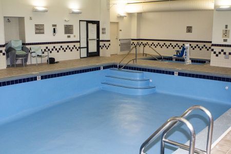 Empty indoor swimming pool with blue water and a metal handrail in a tiled recreation room