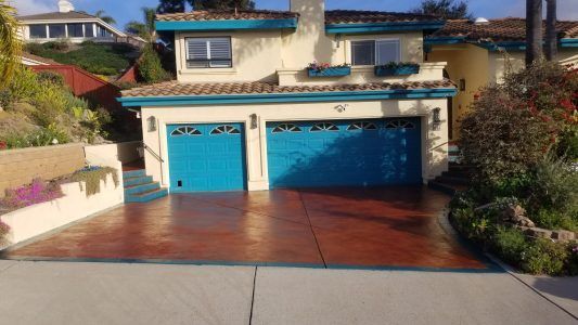 Blue double garage on a hillside home with a red driveway and surrounding greenery