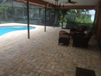 Covered patio with wicker seating beside a screened-in pool area and tiled floor