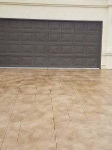 Two-car garage with a closed dark gray door and tan tiled driveway