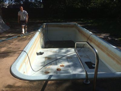 Empty drained swimming pool with a person standing beside it in a sunny backyard