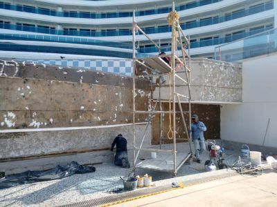 Construction workers on scaffolding repairing a weathered exterior wall in front of a modern building