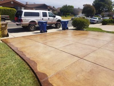 Driveway with a smooth tan stamped-concrete surface, two blue trash bins, and a white SUV parked on the street.