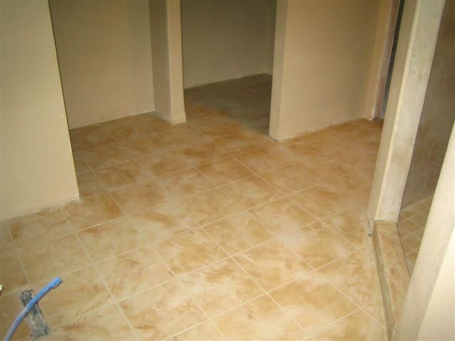 Empty tiled hallway with beige walls and doorways, viewed from a low angle.