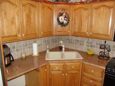 Corner kitchen with oak cabinets, brown countertops, beige tile backsplash, and a white sink.