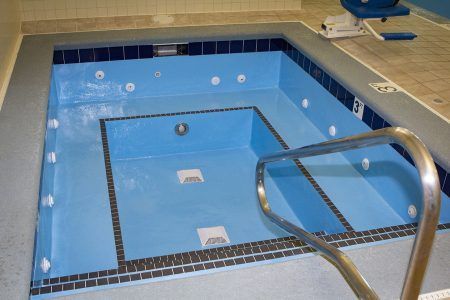 Indoor blue-tiled pool with stainless handrail and steps, likely a spa or therapy pool